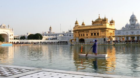 a guard paddles a boat around the pool at golden temple in amritsar, india