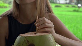 Closeup shot of a young woman drinking young cocnut in a street cafe with a rice field at a background