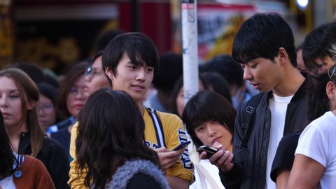 Tokyo / Japan - 10 21 2018: TOKYO, JAPAN, OKTOBER 21 - Static shot of men playing with their phones, in a street full of people, at a autumn day, in Harajuku, Tokyo, Japan