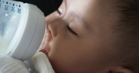 Closeup View of Asian baby girl feeding from a bottle of milk. Baby Eyes closed while feeding.
