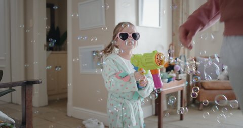 funny little girl blowing bubbles chasing mother with toy gun running through house playing catch happy mom enjoying fun game with daughter enjoying weekend morning 4k footage