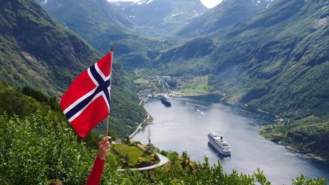 Norwegian flag waving on wind. Fjord Geirangerfjord with cruise ship in the background. View from Ornesvingen viewpoint. Travel for relaxation and sightseeing