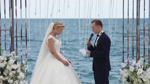 wedding couple speaks laughing at sea under pictorial arch and lady talks into microphone shooting from different angles