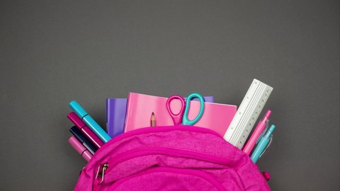 Back to school background in grey-pink colors. Partly view backpack with sticking out school supplies. Stop motion