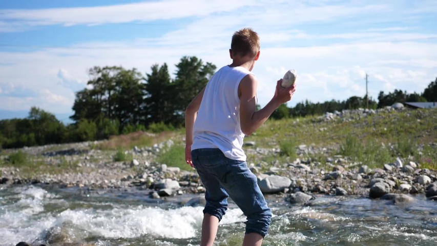 The guy plays on the river Bank, throws stones into the water. Cold mountain river. Outdoor recreation.