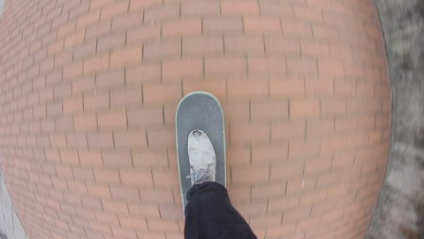 Point of view of skateboarder riding skateboard on the city sidewalk. Skater rolling freestyle in urban environment. Young man holding balance on board, extreme sport

