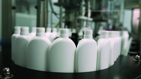 Cosmetics manufacturing plant. White bottles on the belt conveyor. Shampoo, shower gel and lotion.