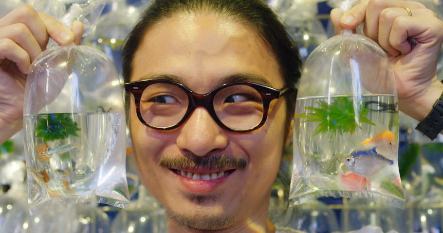 Fun portrait of young trendy asian chinese man with eyes moving from side to side and bags of fishing at the side of his head in Honk Kong. Slow motion, hand held, Shot on red.