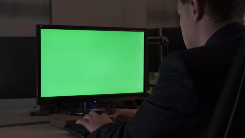 Rear view of a young office male worker sitting at his desk working at computer, chromakey monitor. Stock footage. Office concept with working environment, green screen. | Shutterstock HD Video #1034682740