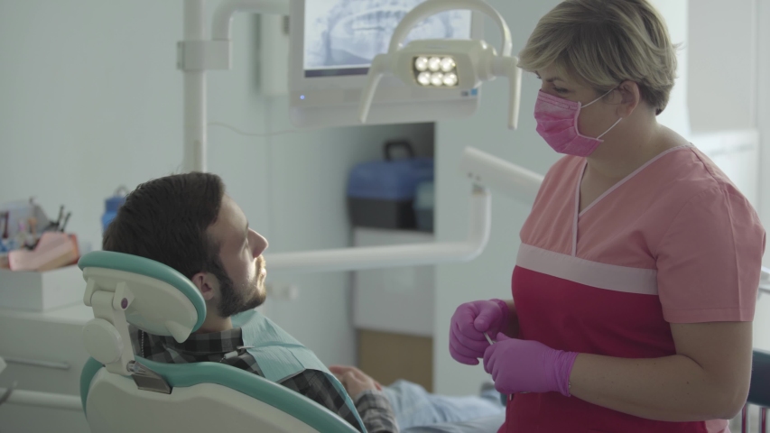Dentist in medical mask and gloves checking condition of her patient using gestures. Female professional doctor stomatologist at work. Dental treatment, medical concept. Dental care. | Shutterstock HD Video #1034687624
