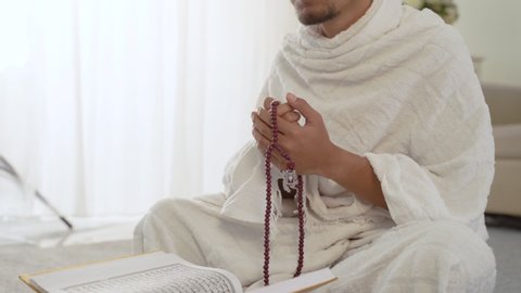 muslim asian man praying with prayer beads while standing in white traditional clothes