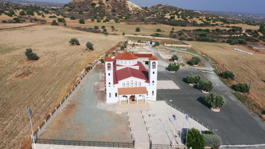 Aerial orbit shot of rural church in Cyprus. Greek and Cyprus flags waving in the wind.