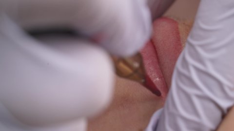 Close-up of patients lips during the procedure of lip blushing with tattoo machine. Permanent cosmetics. Beauty concept