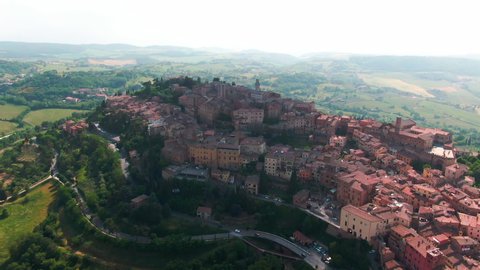 Flying drone over wonderful authentic italian cityscape and green meadows. Aerial view of amazing Montepulciano old town with red rooftops located in highland. Tuscany, Italy