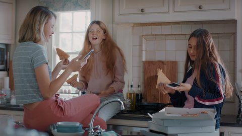 group of teenage girls eating pizza in kitchen having fun chatting together using smartphones sharing lifestyle friends hanging out enjoying relaxing at home