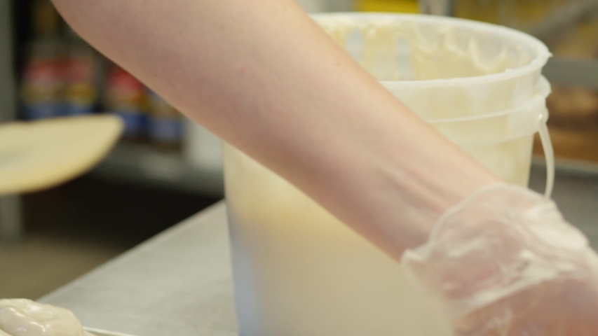 woman puts icing glaze on large cinnamon role with spatula. Woman ices cinnamon rolls with small spatula.