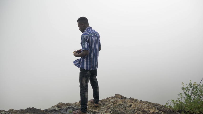 African man standing on the edge of a cliff and looking into a cloudy fog.
