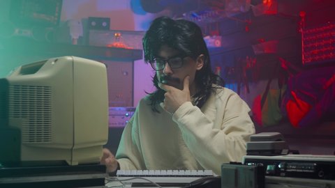 In the '80s or '90s young man thinking about how to solve a problem on his computer. Retro scene with vintage colors and atmosphere.