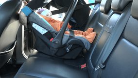 woman fasten baby safety chair with infant child on back leather car seat with safety belt and close door. Safe baby transportation inside automobile. 4K UHD video clip.