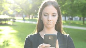 Front view of a serious woman walking in a park using smart phone
