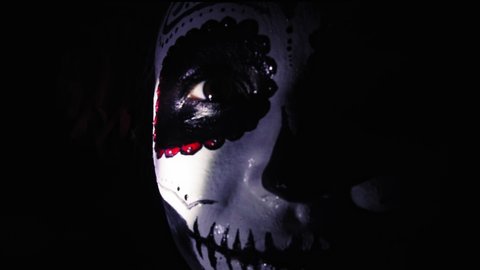 Halloween mask Katrina. A girl in a blinking and frightening light. Mexican day of the dead. Portrait of a young woman with scary makeup for Halloween on a dark background. 4K