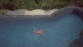 Drone point of view of Young woman floating in star shape in infinity pool in rainforest scenery. Girl enjoys tropical vacations in an idyllic resort 