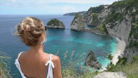 Girl loving tropical paradise. Young woman on top of idyllic beach makes a heart shape with hands showing love to nature and environment-  slow motion 