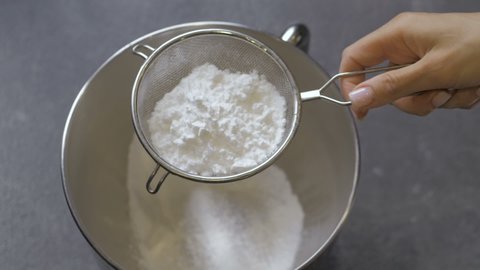 Slow motion of female hands sifting flour by sieve in bowl