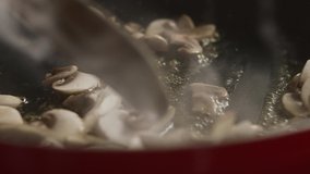 Close-up of chef with wooden spatula interferes with chopped champignon mushrooms in pan. Slow motion video
