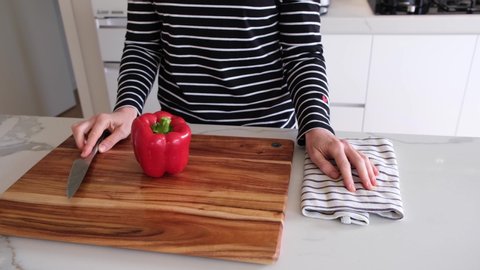Closeup pan of Caucasian woman hands cutting bell pepper on wooden board in a modern kitchen