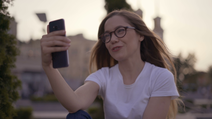 Smiling long-haired girl talking to friends in a video chat using a mobile phone. Girl in the park 4K