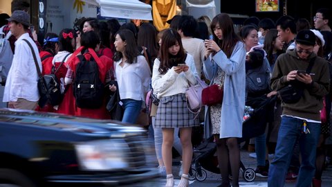 Tokyo / Japan - 10 21 2018: TOKYO, JAPAN, OKTOBER 21 - Static shot of women playing with their phones, in a busy street full of people, cars passing by, at a autumn day, in Harajuku, Tokyo, Japan