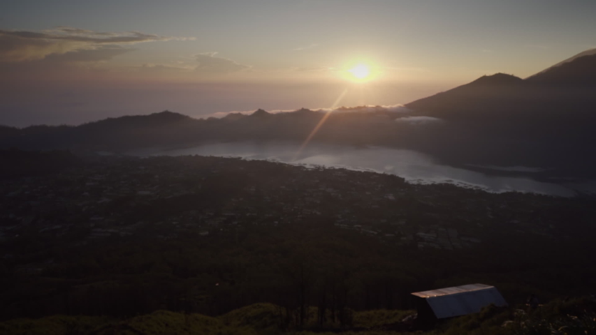 Man hand holds glass with coffee on background of mountains and sunrise. Beautiful view from top of volcano on lake in early morning. Bali, Indonesia
