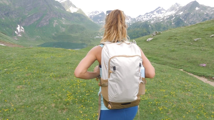 Hiking woman walking above alpine lake on mountain trail contemplating the beautiful landscape in Switzerland; Girl hiking enjoys Summer outdoor activities 