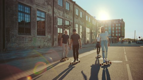Group of Girls and Boys on Skateboards Through Fashionable Hipster District. Beautiful Young People Skateboarding Through Modern Stylish City Street. Moving Slow Motion Portrait Camera Shot