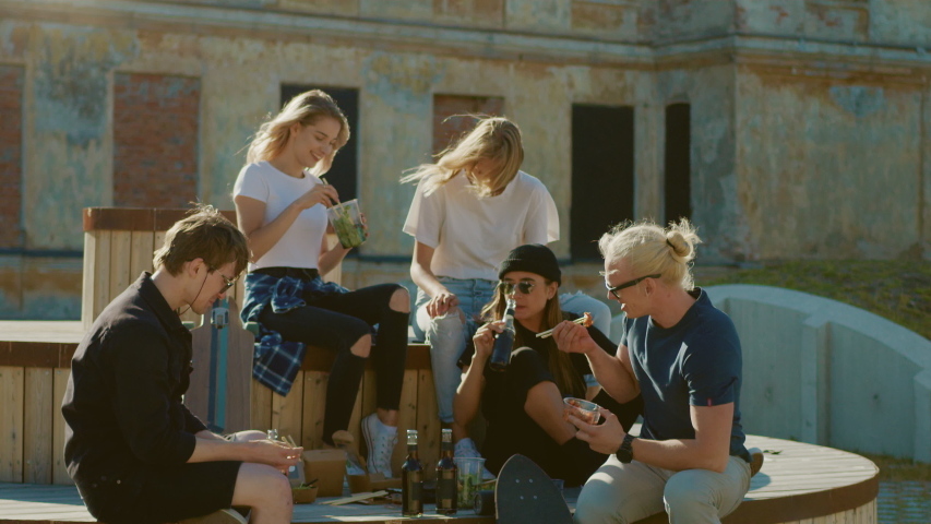 Group of Stylish Girls and Boys Drinking Craft Drinks and Eating Healthy Take Away Street Food on the Park Bench in the Cool Hipster City District. Beautiful Young People Eating Lunch in the Park Royalty-Free Stock Footage #1034749268