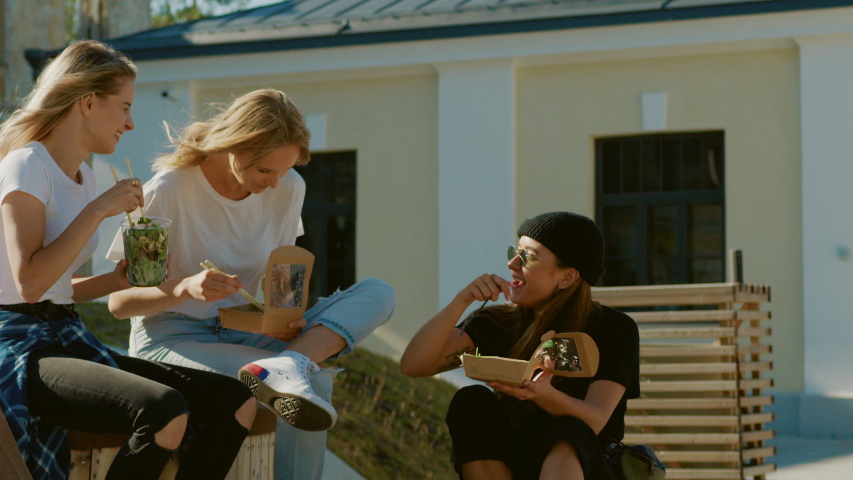Group of Beautiful Girls Eating Take Away Street Food while Sitting on the Bench in the in the Stylish Hipster Part of the City. Three Happy Girlfriends Eating Healthy Foods in the Park Royalty-Free Stock Footage #1034749286