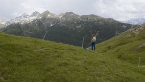 Drone view of girl on mountain top standing arms outstretched celebrating achievement after long day hiking. Young woman arms wide open enjoying freedom; aerial view video 4k  