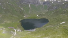 Drone point of view of beautiful alpine lake in Ticino canton in Switzerland; Swiss alps on background and green grass hills; Summer ; Aerial view of heart shape lake 