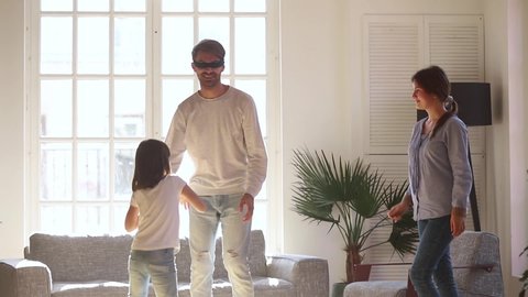 In living room gathered full family preschool adorable daughter spins blindfolded father people starting playing hide and seek game couple and child having fun together at home, enjoy weekend activity