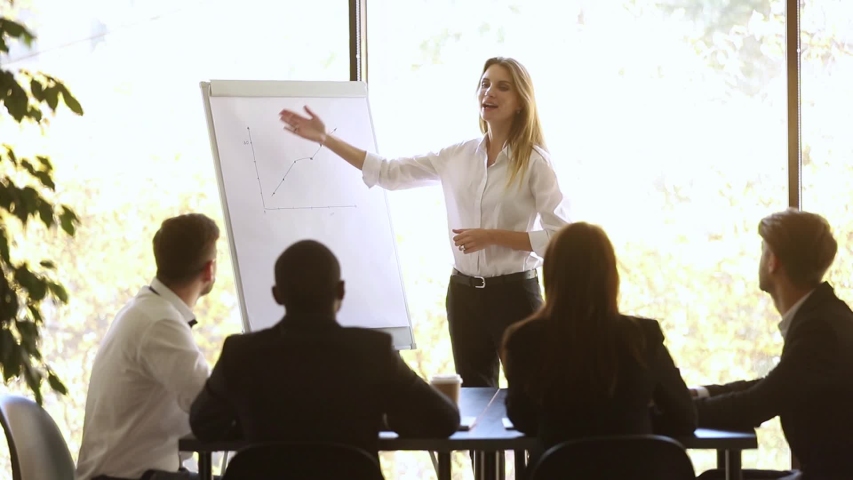 Female coach standing near flip chart showing sales growth during corporate seminar, finish meeting or presentation with positive forecast and participants applauses expressing gratitude and respect Royalty-Free Stock Footage #1034756192