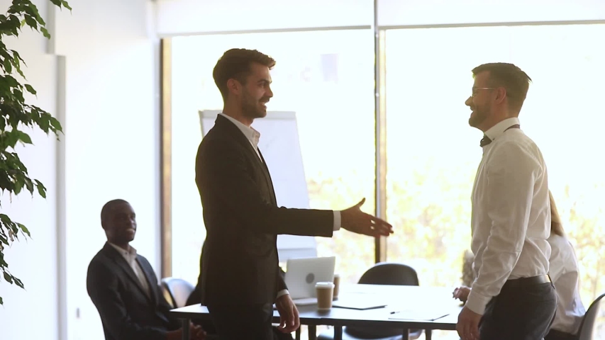 Boss shaking hands welcoming new employee during morning briefing in modern boardroom, diverse staff on background cheers newcomer with applauses, worker of month receive praise gratitude from chief Royalty-Free Stock Footage #1034756237