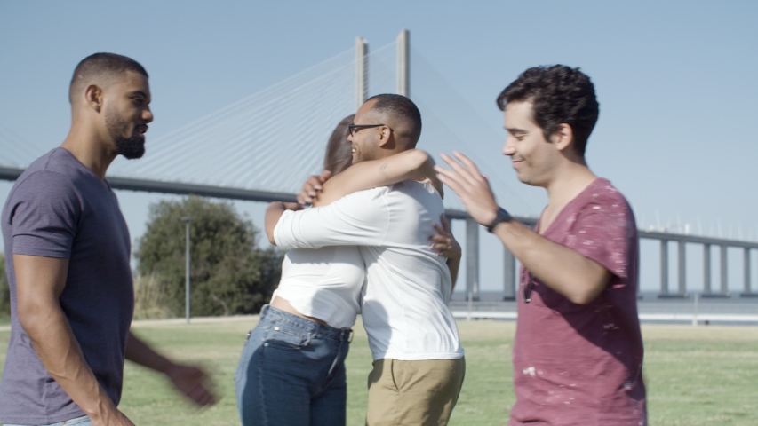 Happy friends greeting each other in park. Smiling stylish people hugging in park. Union concept