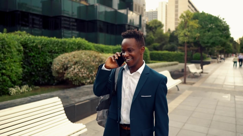 African American businessman wearing blue suit, walking and using modern smartphone near office. Business concept | Shutterstock HD Video #1034757350