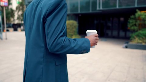 African American businessman wearing blue suit drinks coffee near office. Business concept