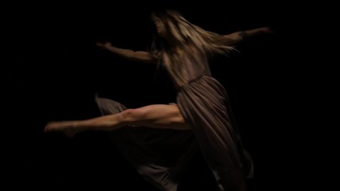 Close-up slow motion of a talented lady performing contemp in the darkness of a studio. She is doing the elements of dance in a twilight against a black background.