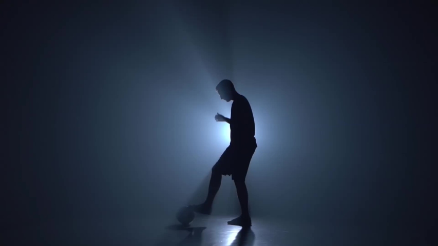 Silhouette of football freestyler stuffing the ball and making tricks in a twilight against a light of studio. Slow motion | Shutterstock HD Video #1034762798