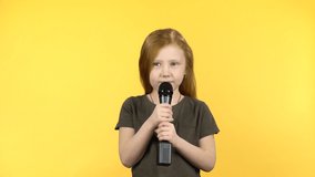 Sweety kid female smiling and singing with microphone doing a little dance on yellow background.