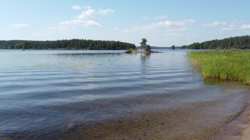 Lake Saimaa in Taipalsaari, near Lappeenranta, Finland. Sand beach on beautiful summer day. Tiny island on background. Clear water with small waves.