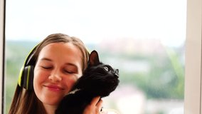 young girl in headphones hugs a black cat happy